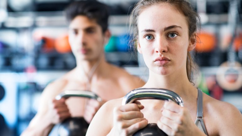 Young fit couple in gym exercising with kettlebell.